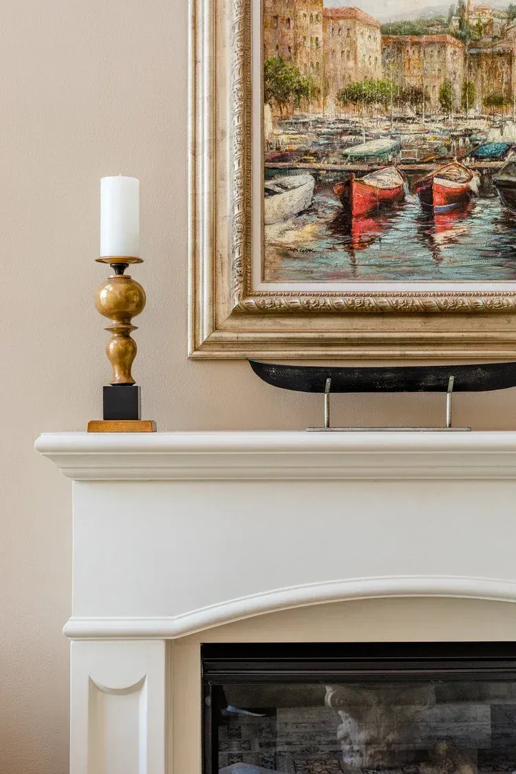 White mantel with brass candlestick and framed harbor painting above a fireplace