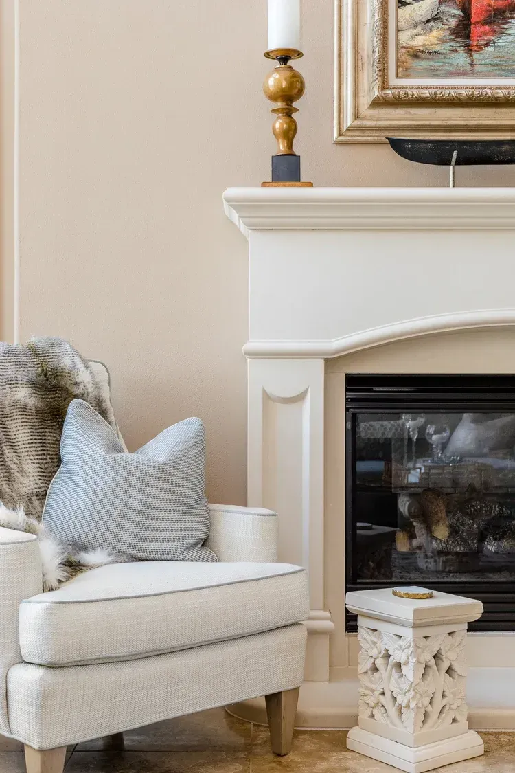 Cozy living room corner with a white armchair, fireplace, and decorative candle and pillow
