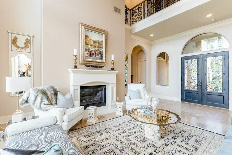 Bright living room with a white fireplace, patterned rug, and blue double front doors beside arched windows.