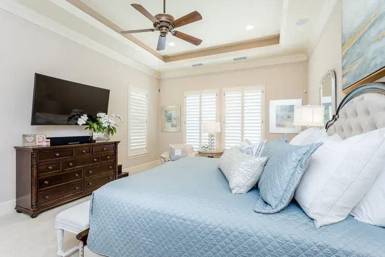 Bright bedroom with a blue bedspread, dresser with TV, and ceiling fan