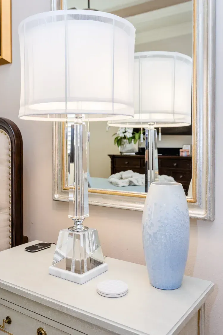 White table lamp and blue vase on a mirrored console table with a framed mirror behind them