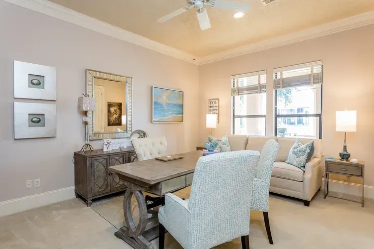 Bright living room with beige sofa, blue chairs, wooden table, and soft lamp lighting.