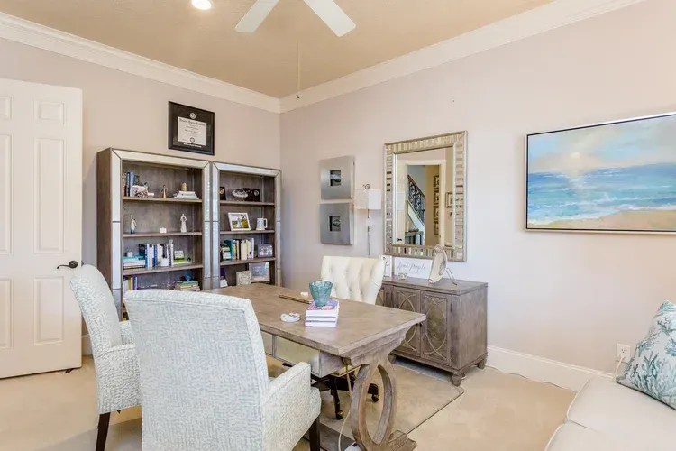 Bright dining room with white chairs, wooden table, mirrored cabinet, and beach painting on beige walls
