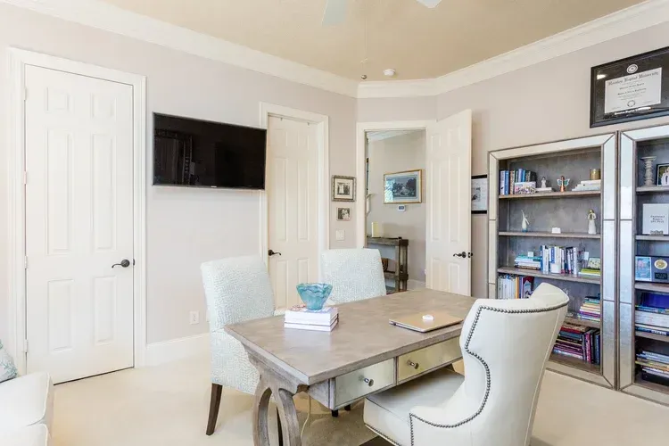 Bright dining room with a table, chairs, wall-mounted TV, and bookshelf near an open doorway.