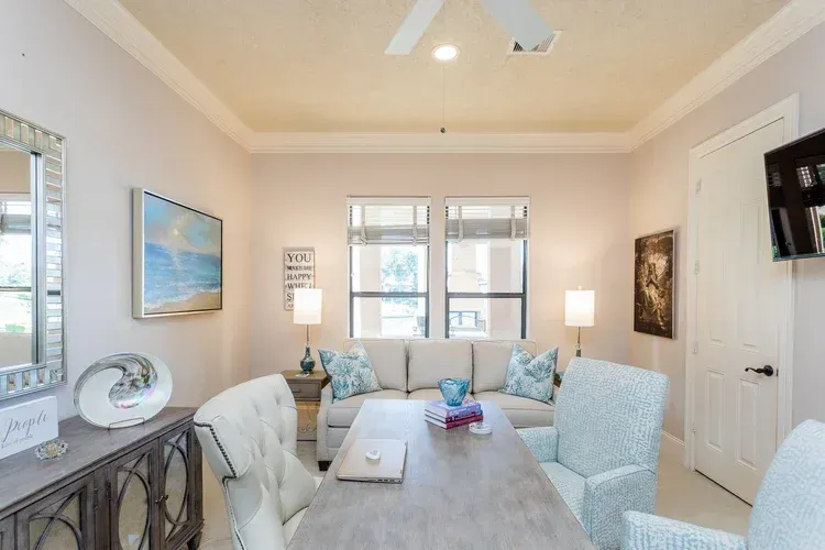Bright living room with light blue chairs, gray sofa, ceiling fan, and wall-mounted TV.