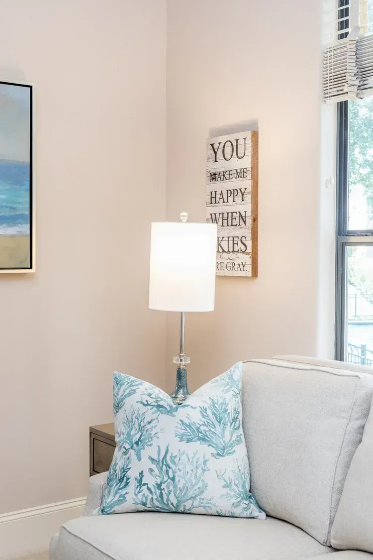 Living room corner with gray sofa, blue patterned pillow, lamp, and wall art by a window