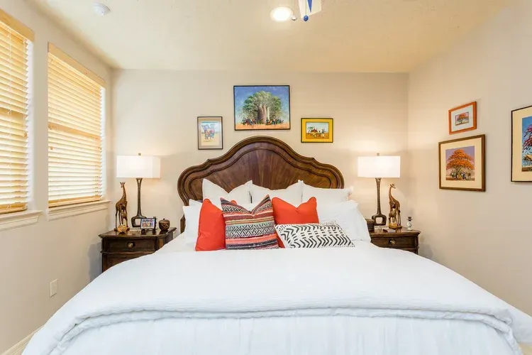 Cozy bedroom with carved wooden bed, white bedding, red pillows, and framed art on cream walls
