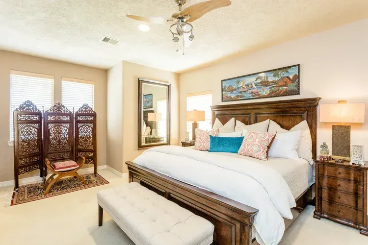Bright bedroom with a wooden bed, bench, nightstands, and a decorative room divider by the window