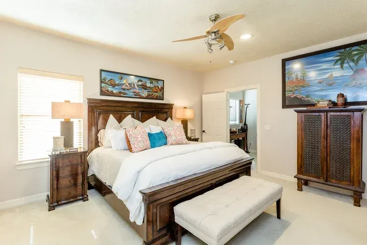 Bright bedroom with a large bed, wood furniture, tropical wall art, and a bench at the foot of the bed