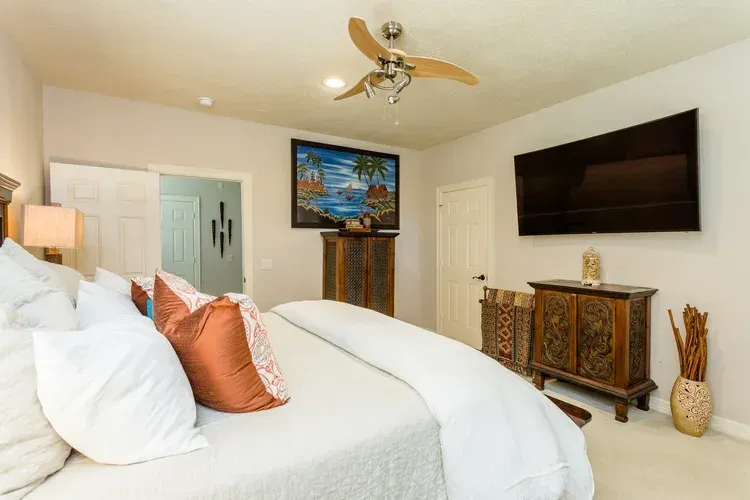 Bright bedroom with a bed, wall-mounted TV, dresser, ceiling fan, and ocean-themed decor