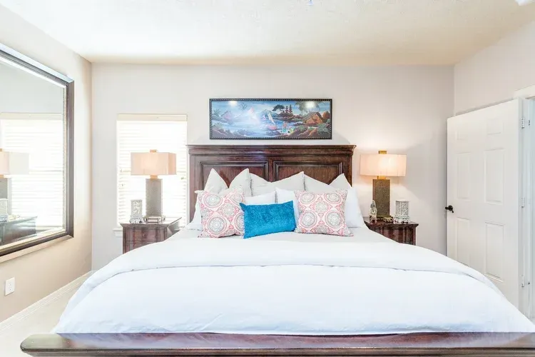 Bright bedroom with a large bed, white bedding, bedside lamps, and framed art above the headboard