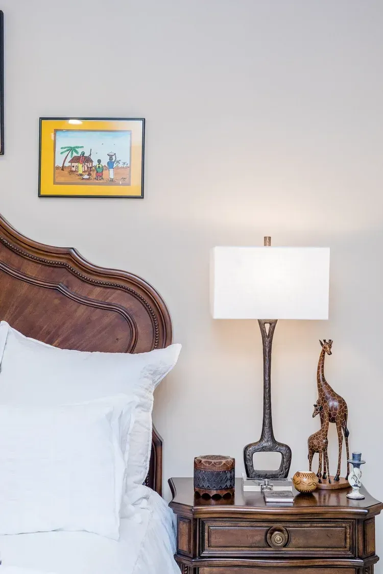 Bedroom with white bedding, carved headboard, bedside lamp, and giraffe figurine on a wooden nightstand