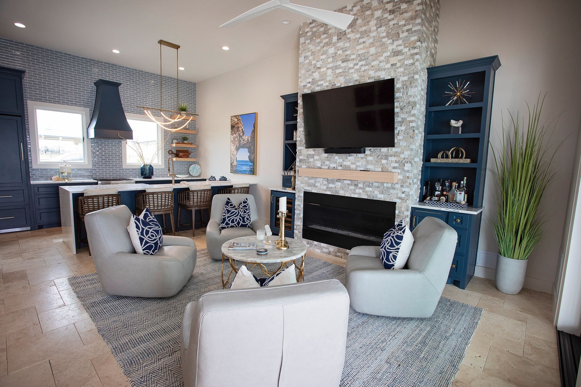 Modern living room with blue chairs, fireplace, wall-mounted TV, and open kitchen in the background