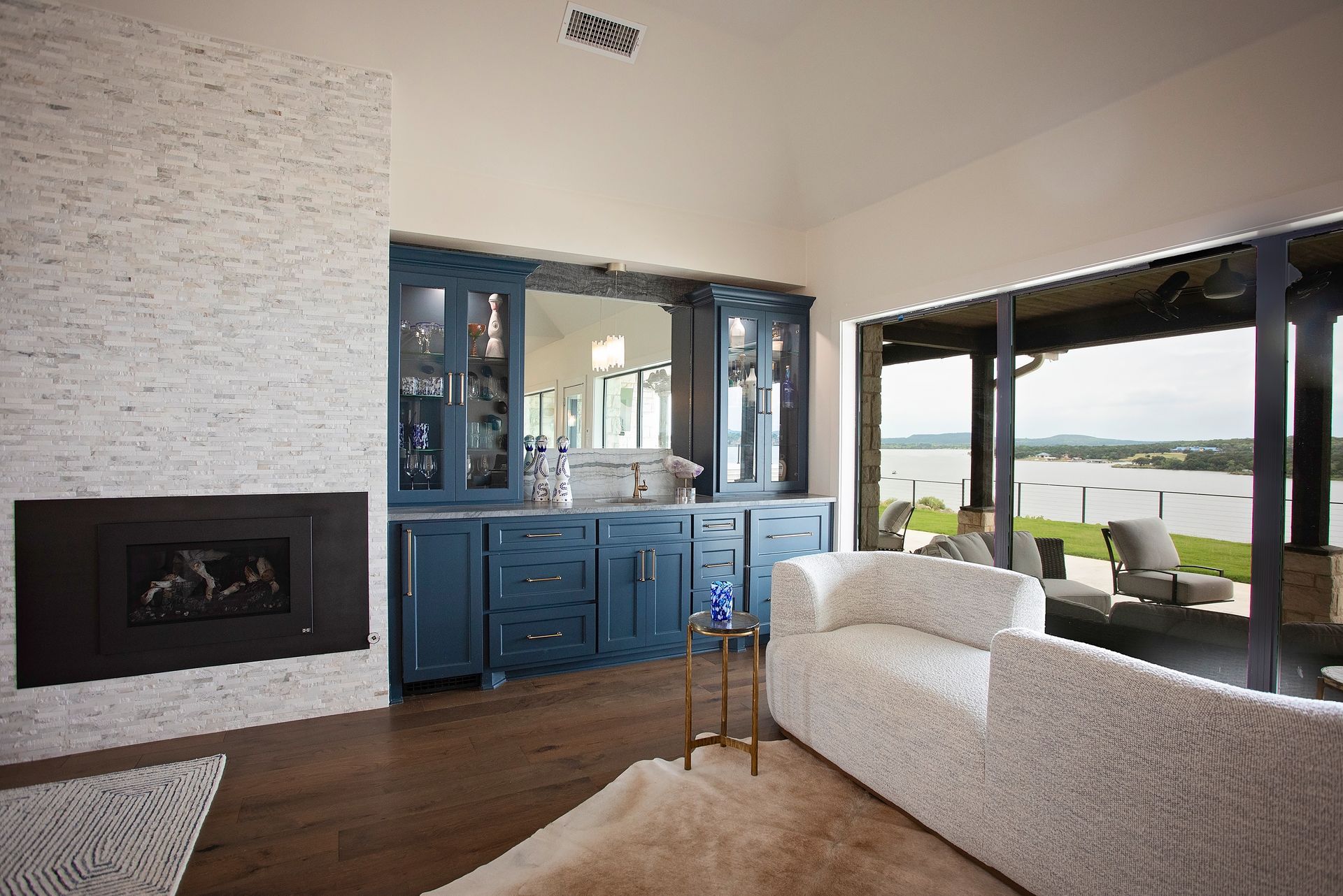 Modern living room with blue cabinet, fireplace, beige sofa, and water view through sliding glass doors