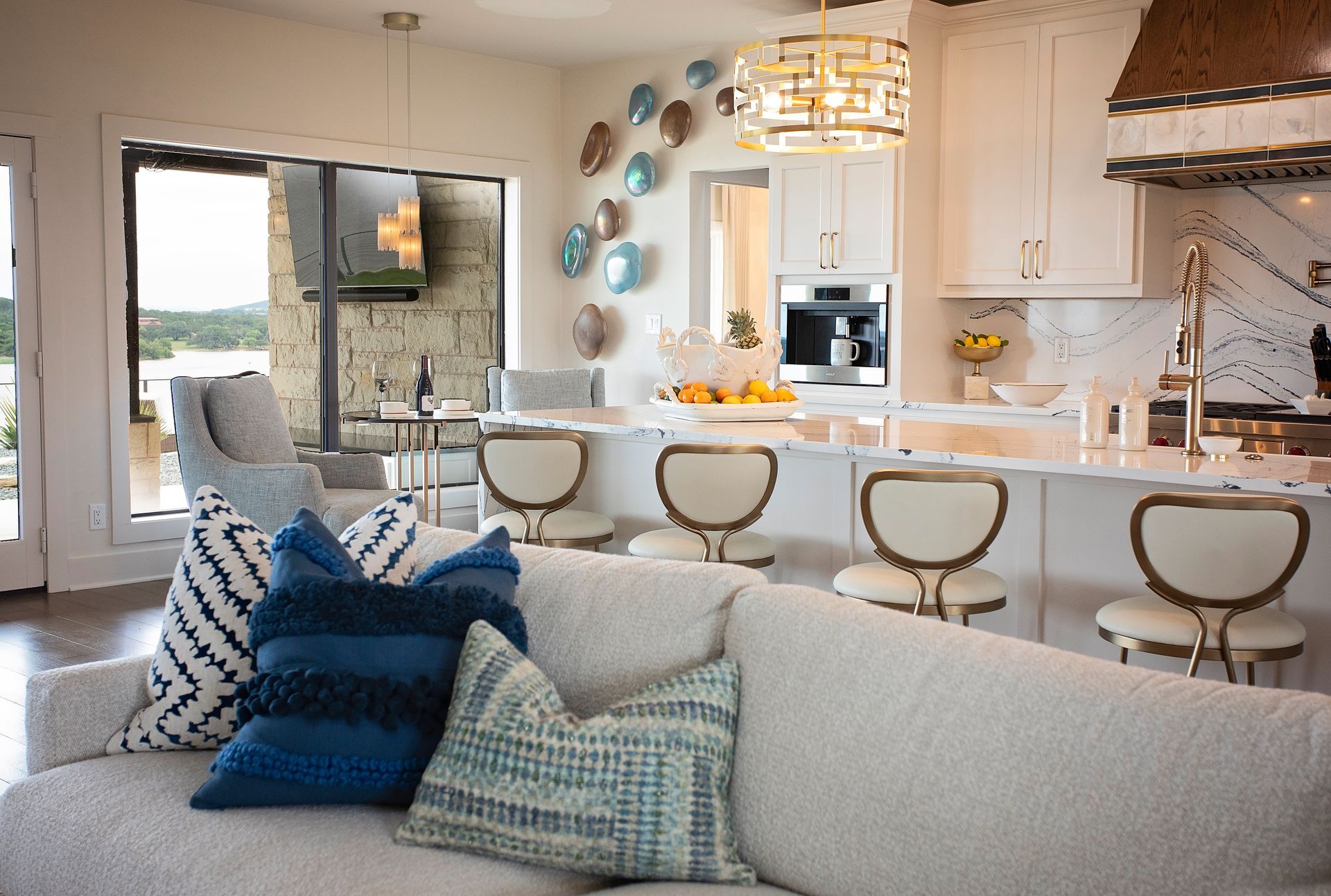 Bright modern kitchen and living room with white island, gold stools, and blue accents on a sofa