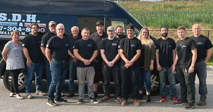 A group of people standing in front of a black van with company logo. They are wearing black shirts and smiling.