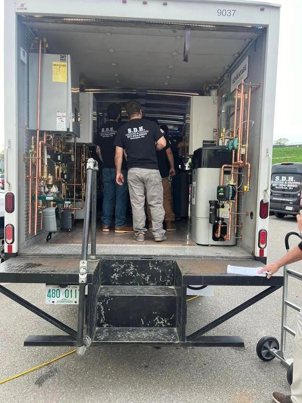 People inside a trailer showcasing plumbing equipment with copper pipes. License plate visible.