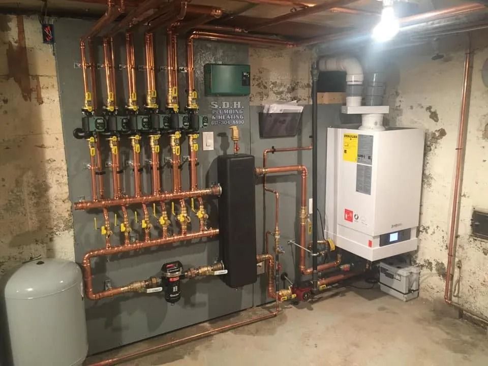Copper pipes and heating system components mounted on a gray wall in a basement.