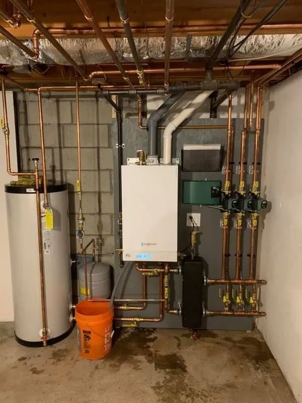 Copper pipes and a boiler system in a basement setting. Includes a water heater and other mechanical equipment.