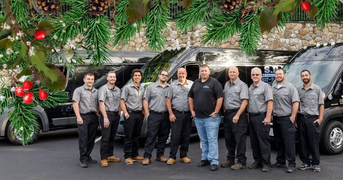 Group of men in work uniforms standing in front of vans, Christmas decorations in the background.
