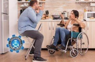 A man sits on a stool and a person sits in a wheelchair in a kitchen, engaged in a conversation with hand gestures.
