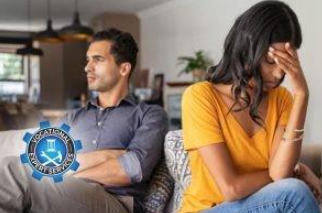 Two people sit on a couch in a living room, looking away from each other with frustrated expressions.