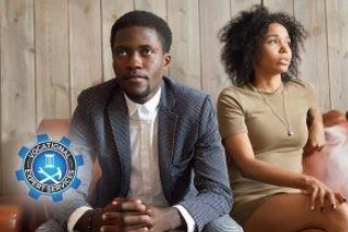 A man in a suit and a woman in a dress sit side-by-side.