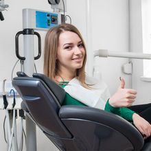 A woman is giving a thumbs up while sitting in a dental chair