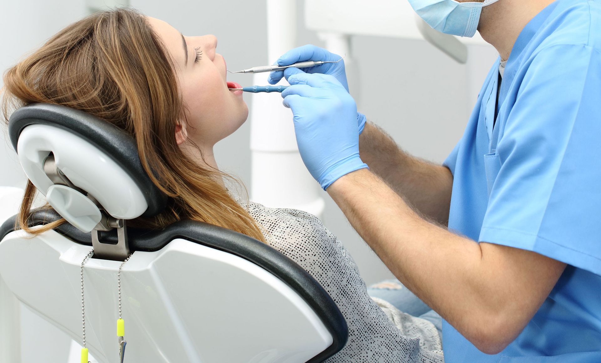 A woman is sitting in a dental chair while a dentist examines her teeth.
