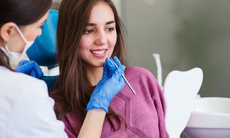 A woman is sitting in a dental chair while a dentist examines her teeth.