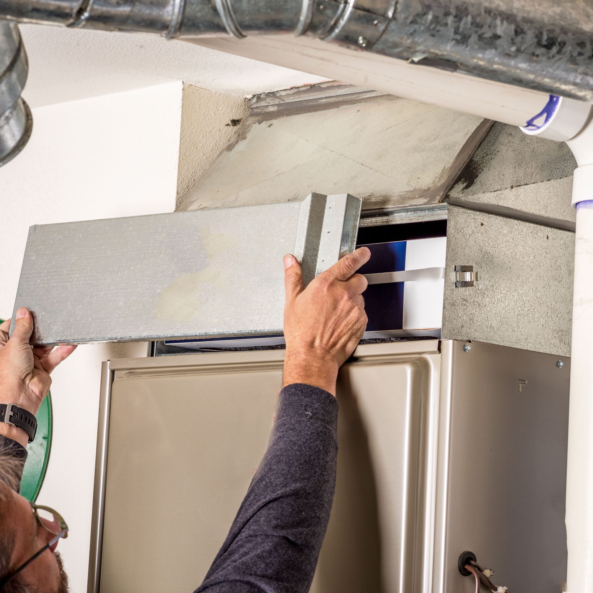 Technician installing a large gray HVAC duct section above a doorway in an unfinished ceiling area