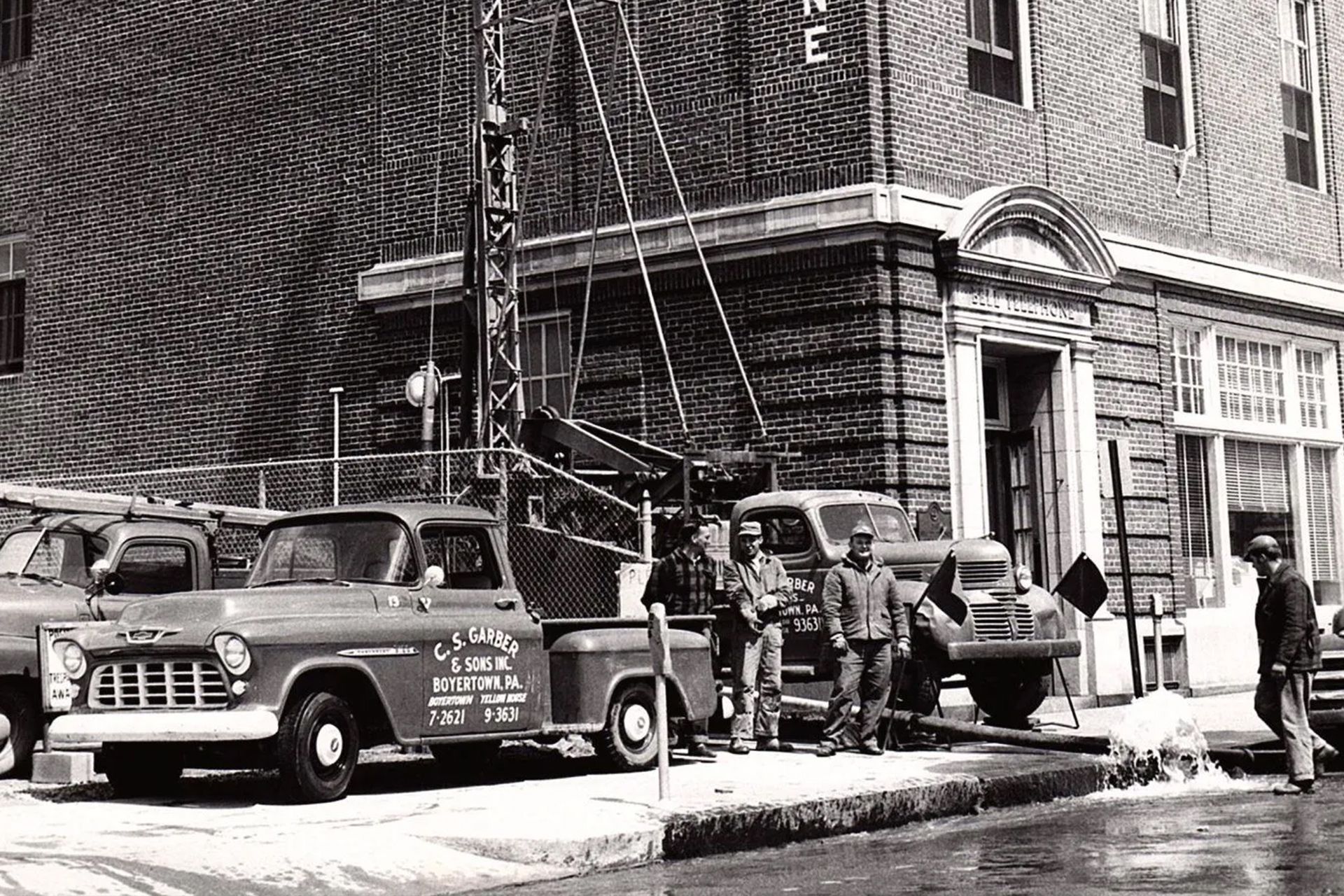 A black and white photo of a building with a truck parked in front of it.