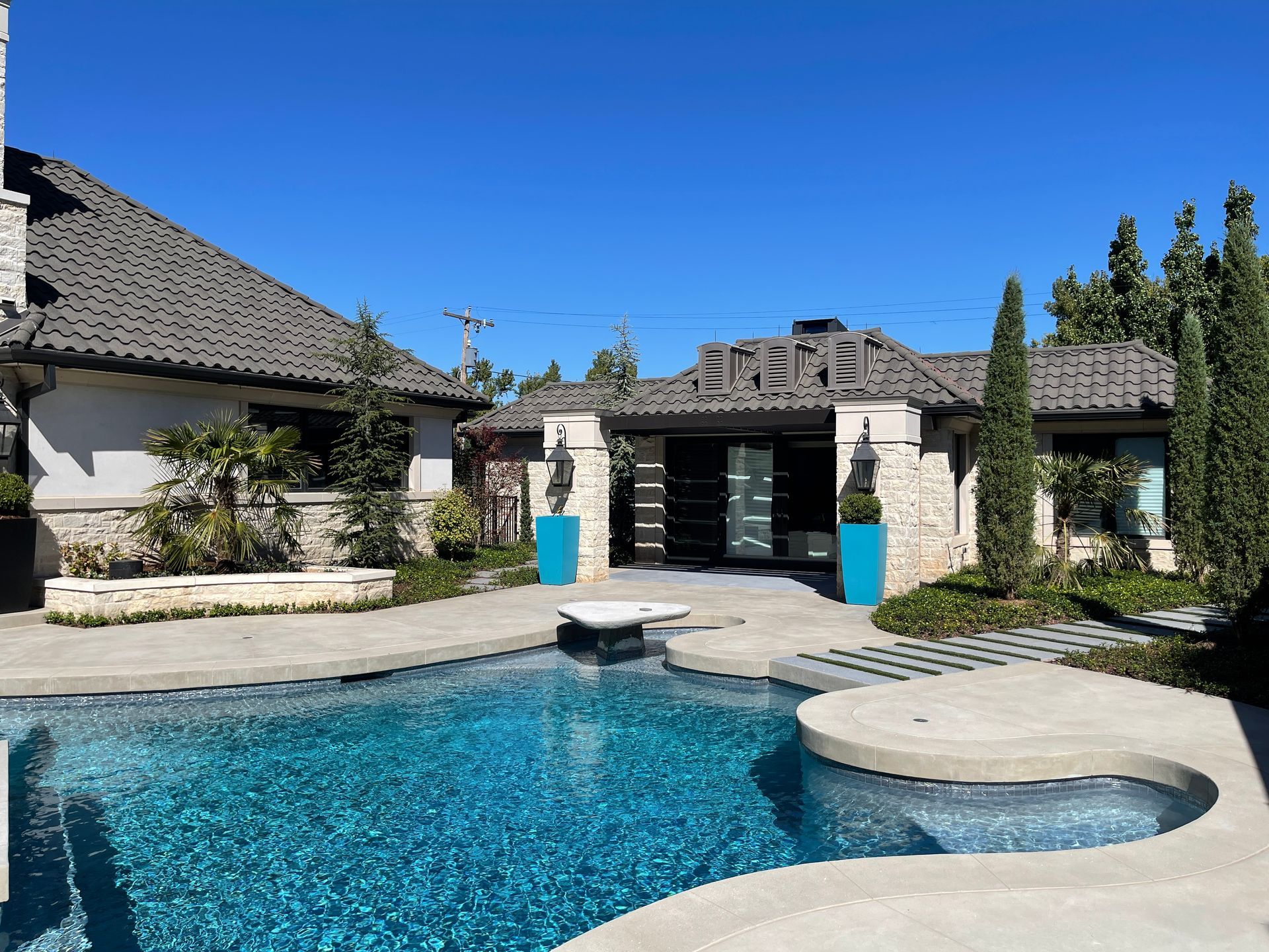 Pool area with a turquoise pool, patio, and stone buildings under a blue sky.