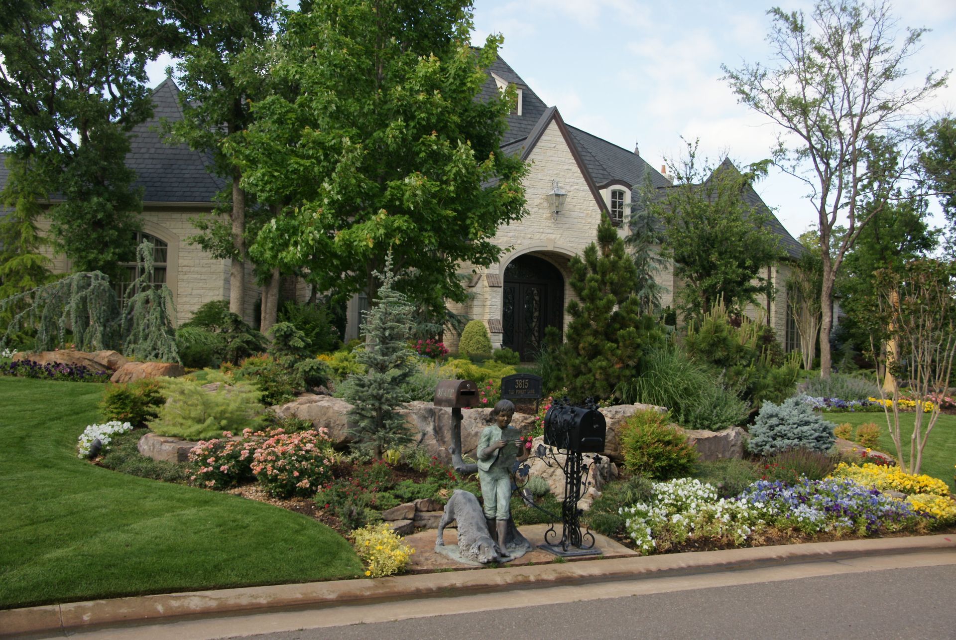 House with lush landscaping and stone facade. A mailbox stands in front with a decorative statue.