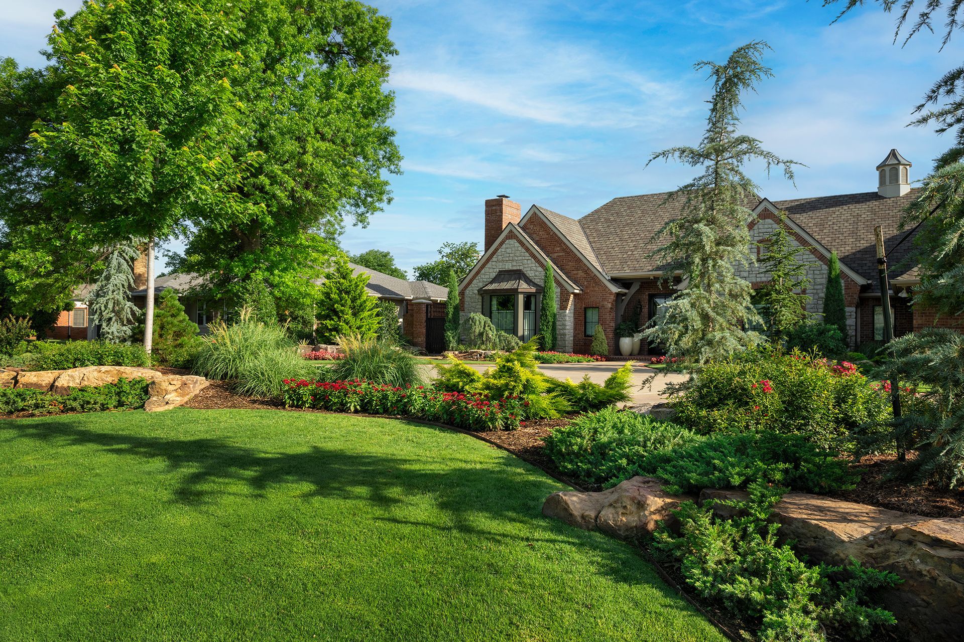 A large, brick house with a well-manicured lawn and garden under a bright, sunny sky.