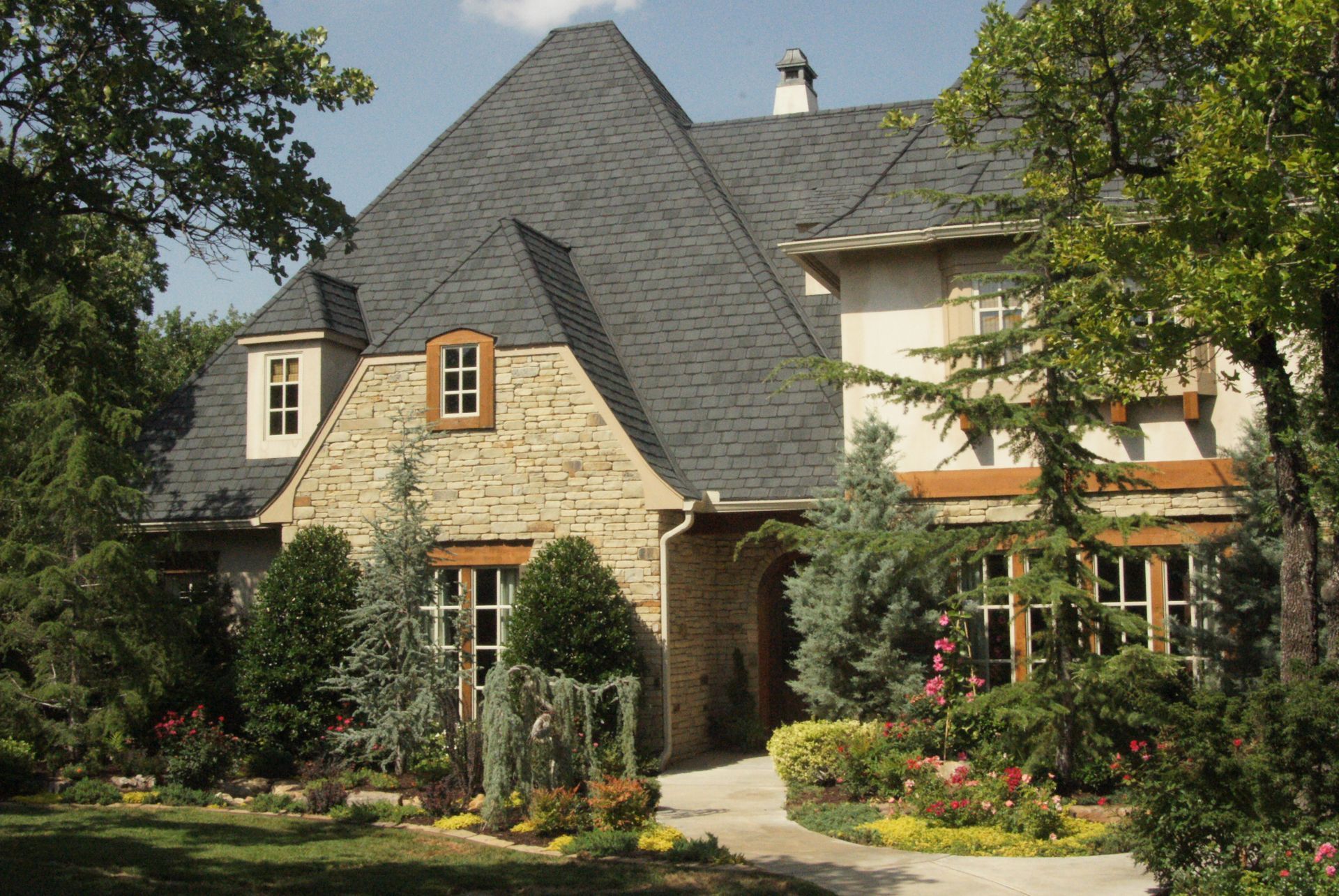 Elegant brick and stucco house with dark roof, surrounded by landscaping and trees.