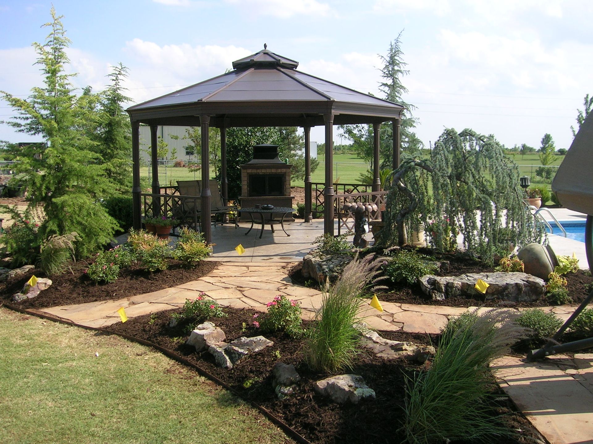 Gazebo with a brown roof and a flagstone path surrounded by landscaping.