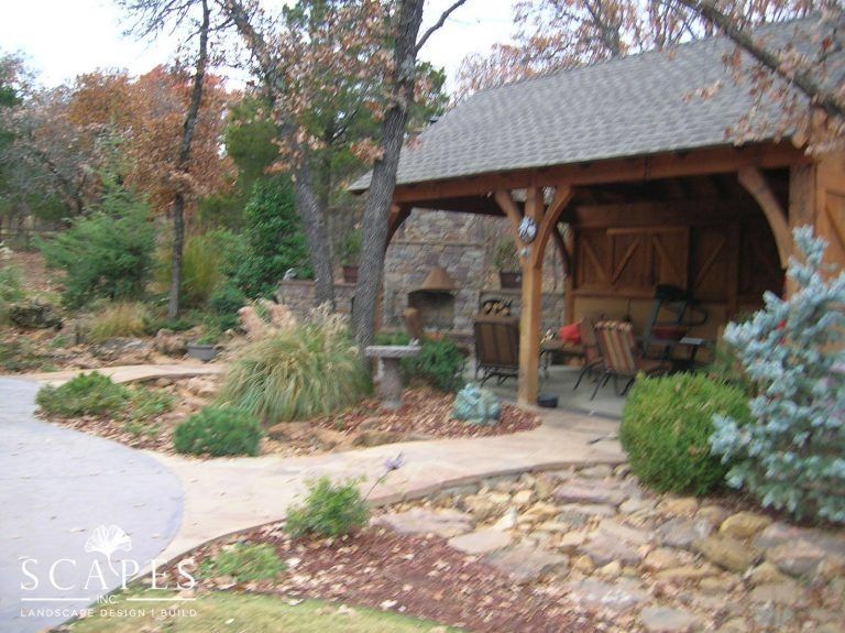 A stone and wood outdoor structure with seating, surrounded by landscaping and a curving driveway.