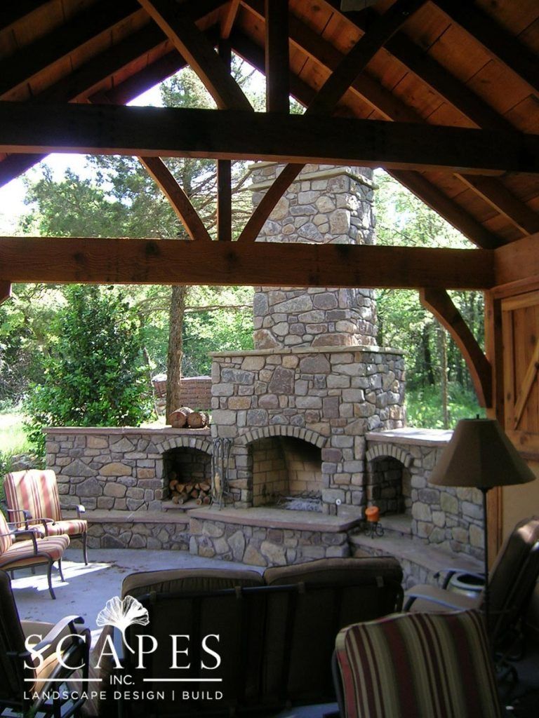 A stone fireplace in an outdoor pavilion. The space features wooden beams, seating, and an inviting ambiance with views of the surrounding greenery.