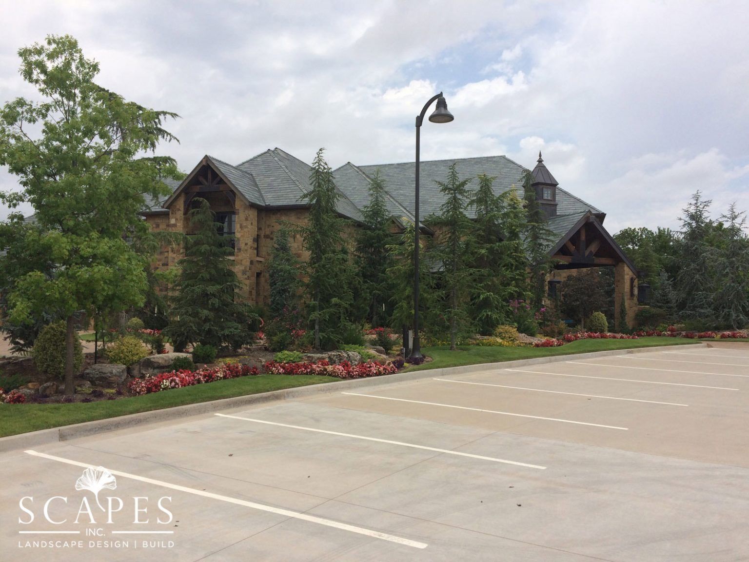 Exterior view of a stone building with a dark roof, surrounded by landscaping and a parking lot on a cloudy day.
