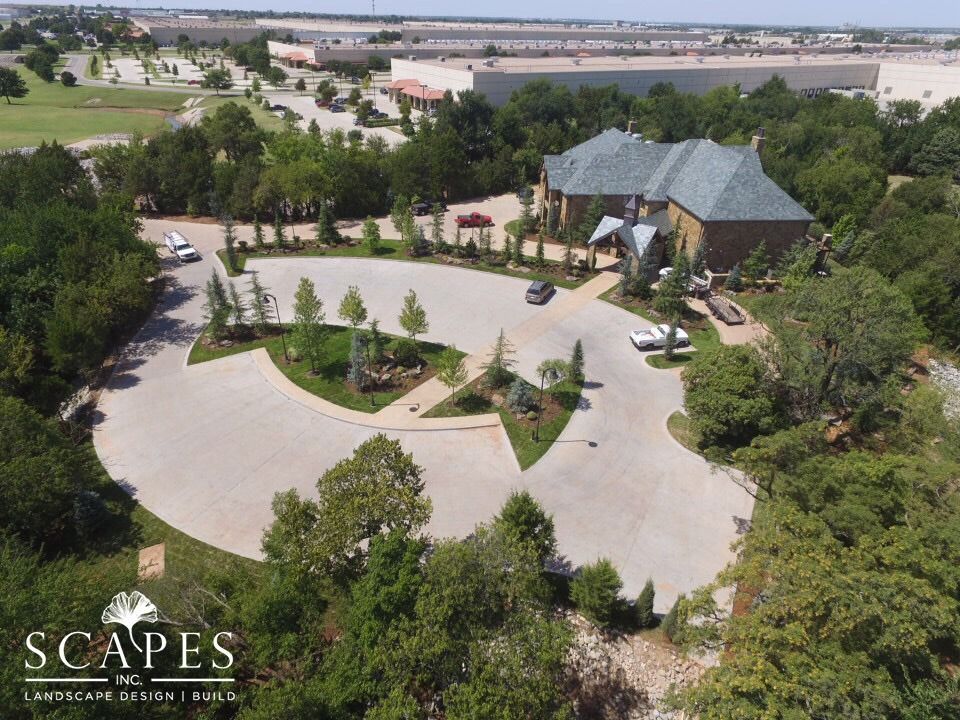 Aerial view of a large house with a circular driveway and landscaping. Green trees and shrubs surround the property.