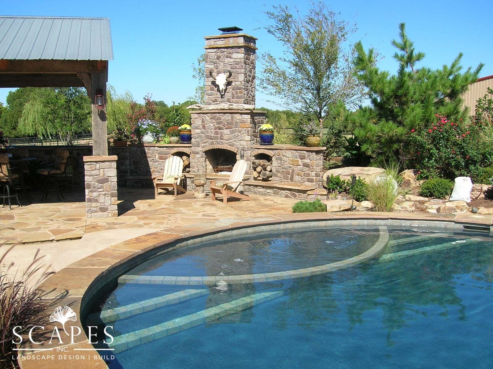 Stone fireplace and pool area with lounge chairs, under a blue sky.