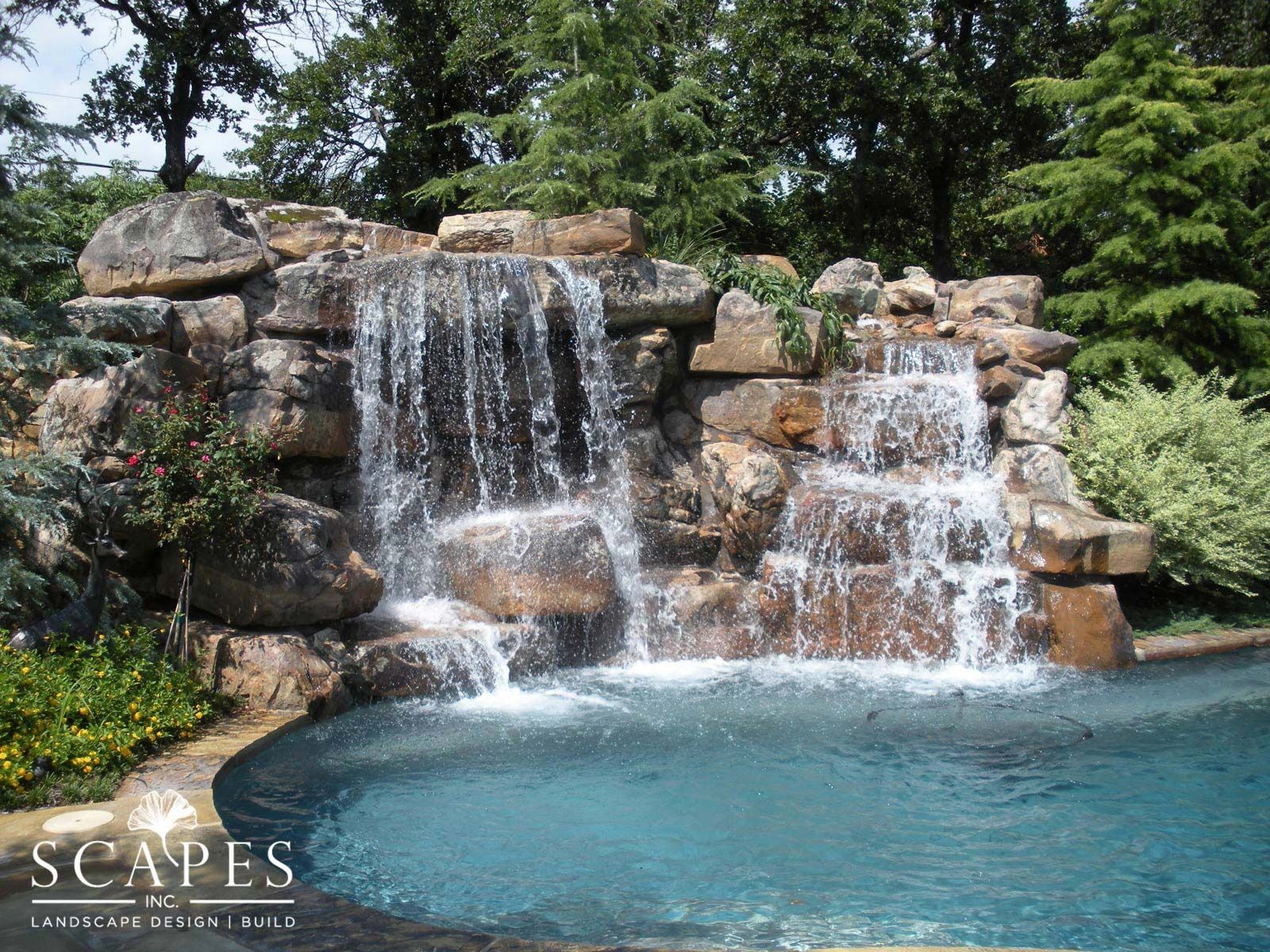 Waterfall cascading over rocks into a blue pool, surrounded by greenery.