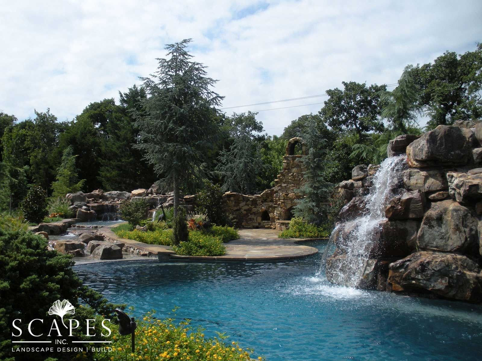 Pool with waterfalls cascading over large rocks surrounded by trees and greenery.