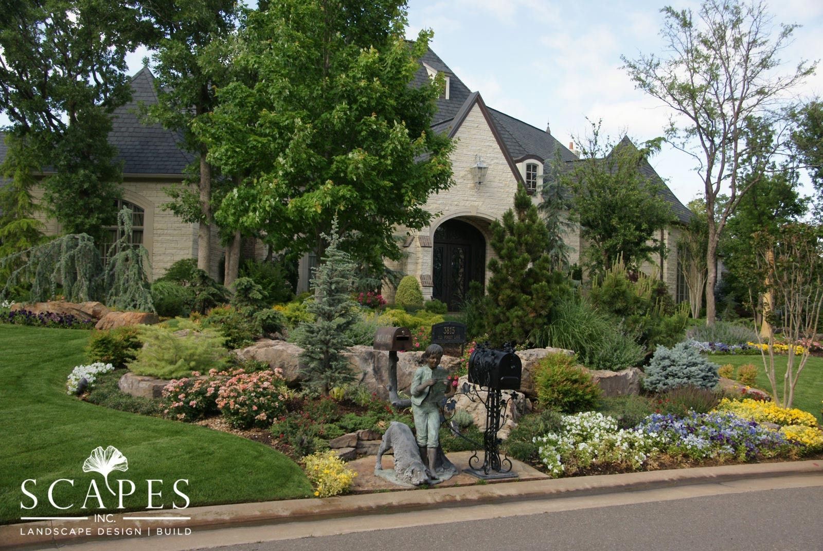 A stone house with lush landscaping, featuring a statue and mailbox near the street.