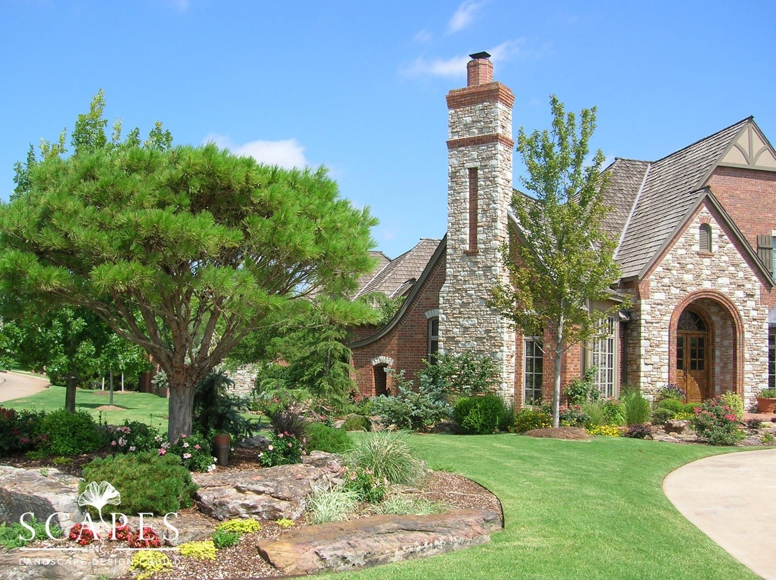 Stone and brick house with lush green lawn and landscaping under a blue sky.