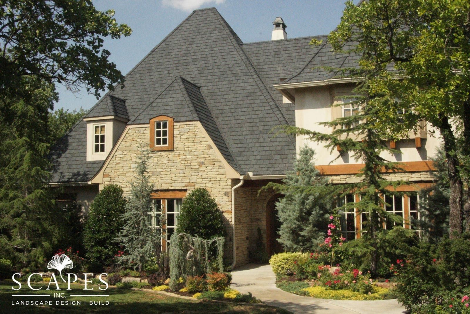Stone and stucco house with a dark gray roof, surrounded by landscaping.