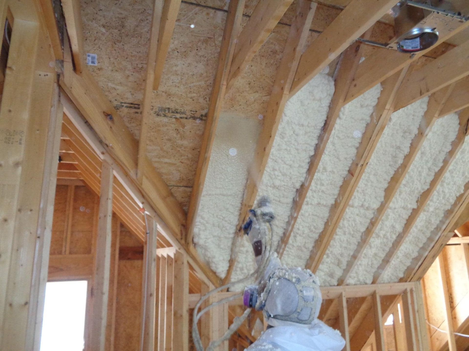 A person is spraying foam on the ceiling of a house under construction.