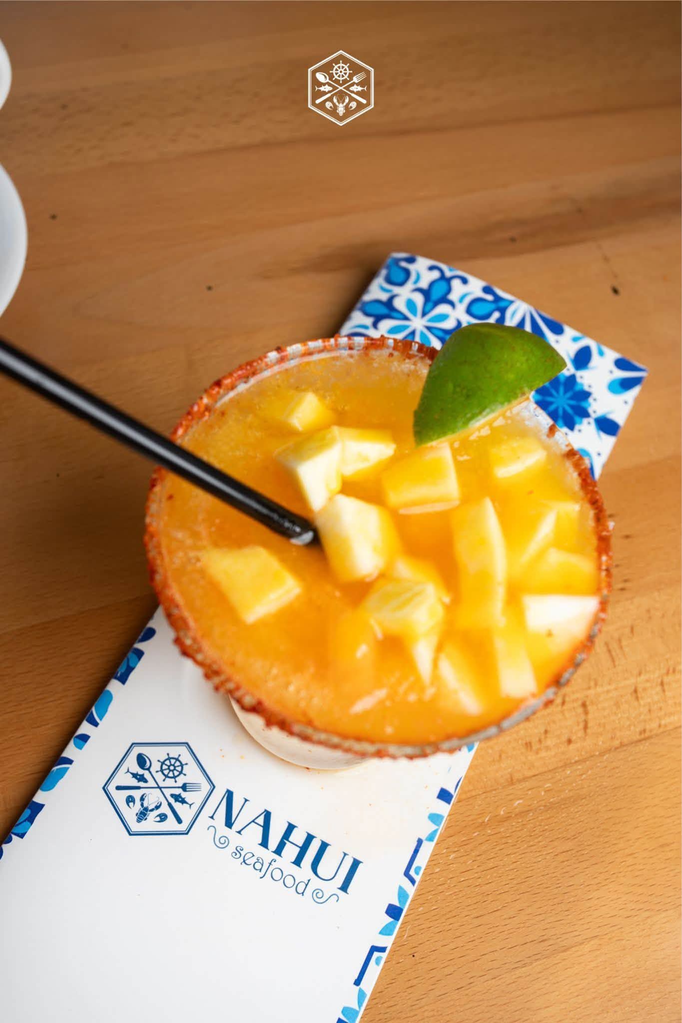 Tropical orange cocktail in a glass with pineapple chunks, mint, and a black straw on a restaurant table