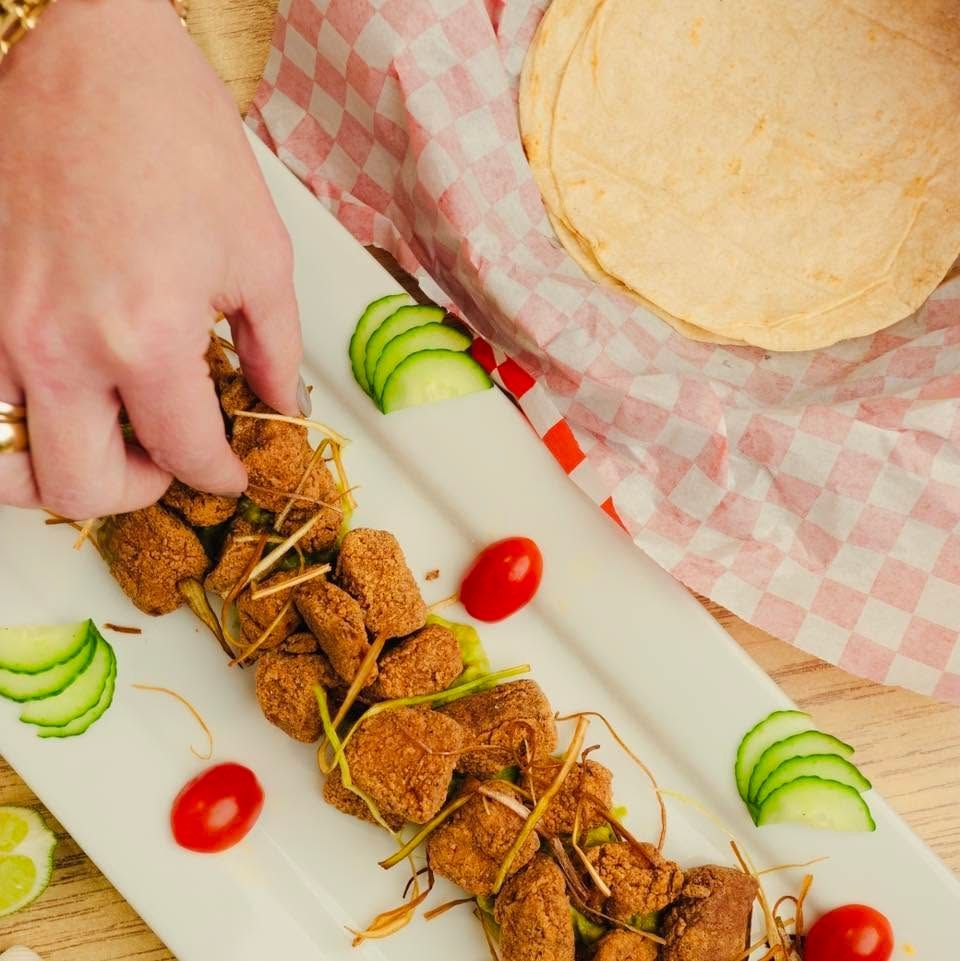 Hand arranging stuffed baked rolls on a white platter with cucumber slices and cherry tomatoes